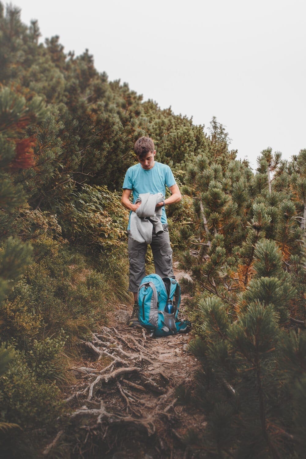 Boy packing his clothes to backpack on trail