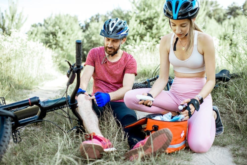 Woman giving first aid to a man with knee injury while cycling on the mountain bicycles on the forest road during the summer time