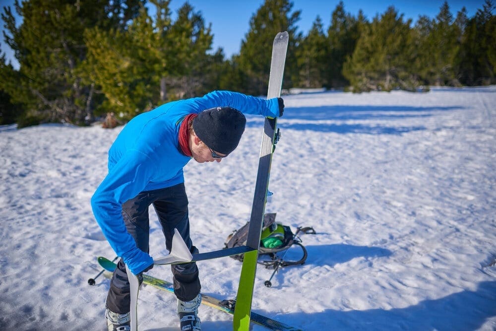 Backcountry Skier sticking climbing skins on skis in the snow.
